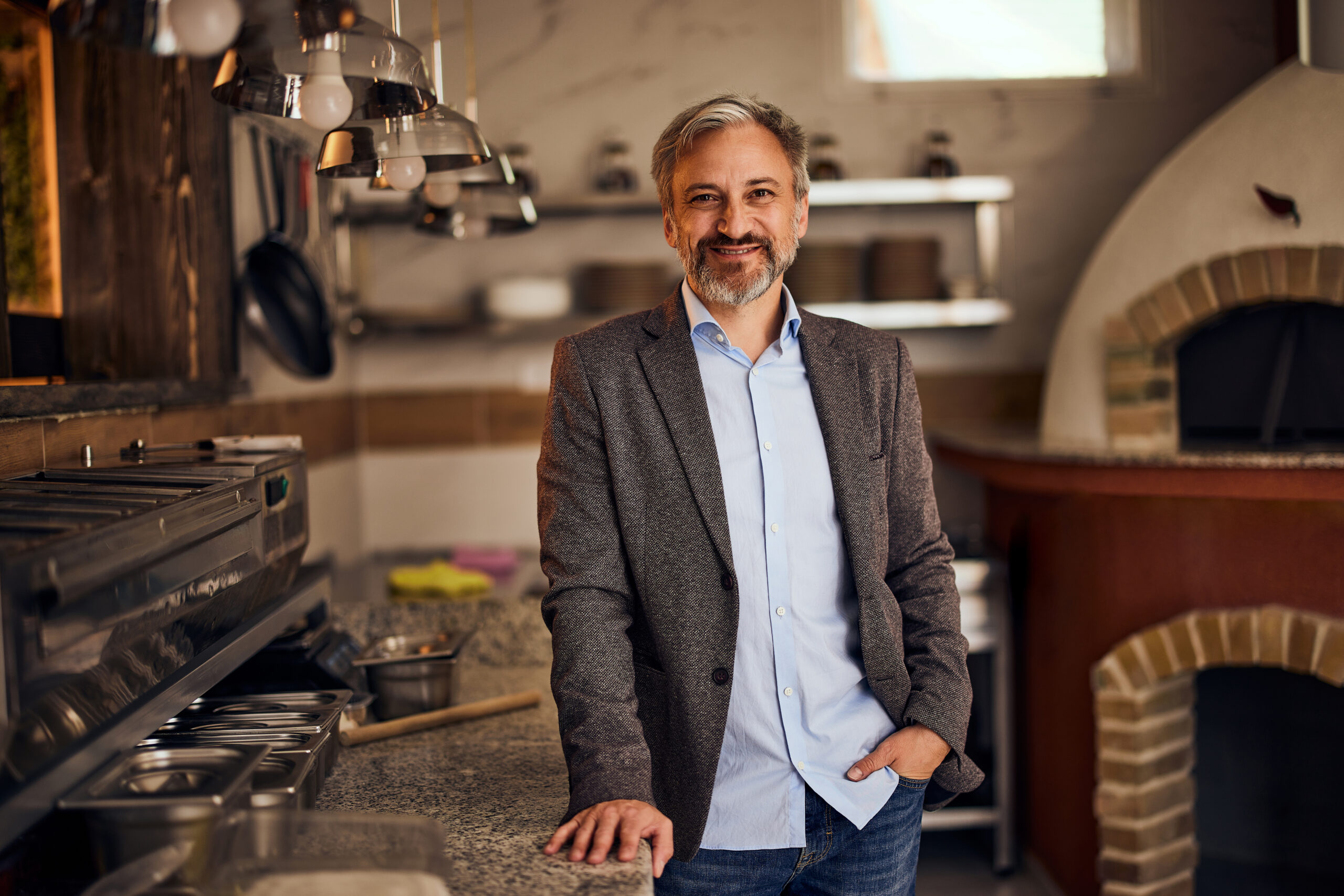 Portrait of a senior businessman, owner of a pizzeria restaurant, standing in the kitchen, elegantly dressed.
